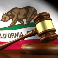 California law, legal system and justice concept with a 3d render of a gavel on a wooden desktop and the Californian flag on background.